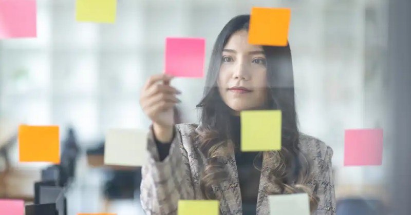 woman placing sticky notes on a clear board